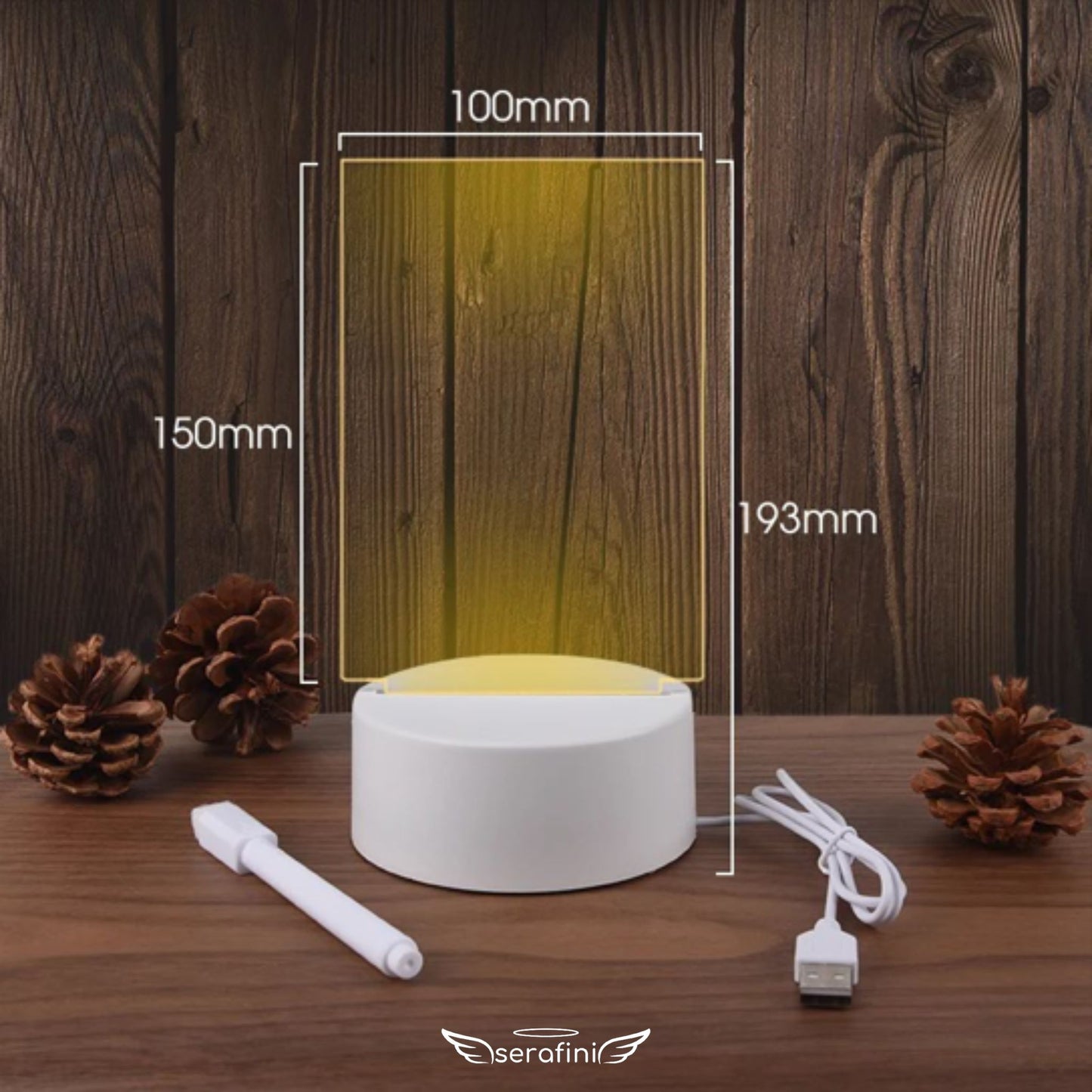 Foto mostrando medidas da Lousa Criativa em formato vertical: 150mm de altura por 100mm de largura o display de acrílico transparente. Altura total incluindo a base: 193mm. Na imagem aparece o cabo carregador e a caneta borracha.