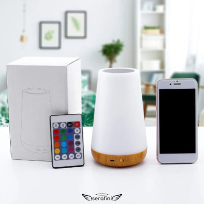 Foto da luminária em cima de um móvel branco, com a caixa ao lado e o controle remoto enconstado na caixa e um celular branco ao lado.